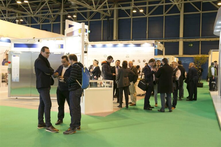 Profesionales del sector de la construcción conversando en los pasillos de una feria, junto a los stands de expositores